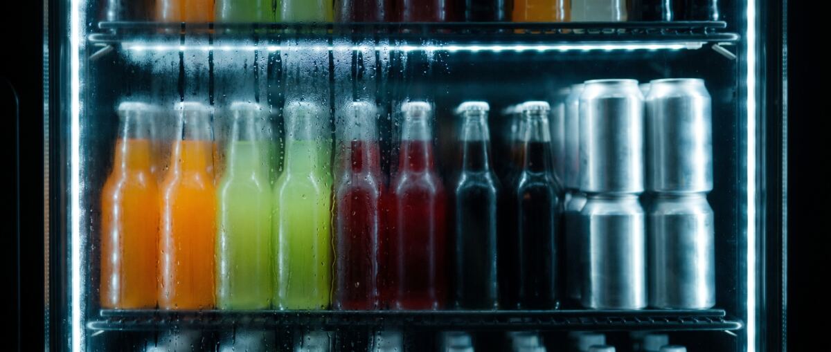 Cold bottles and cans behind a fogged cooler door